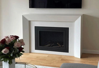 Simple white concrete fireplace surround and black gas fireplaces in a living room.